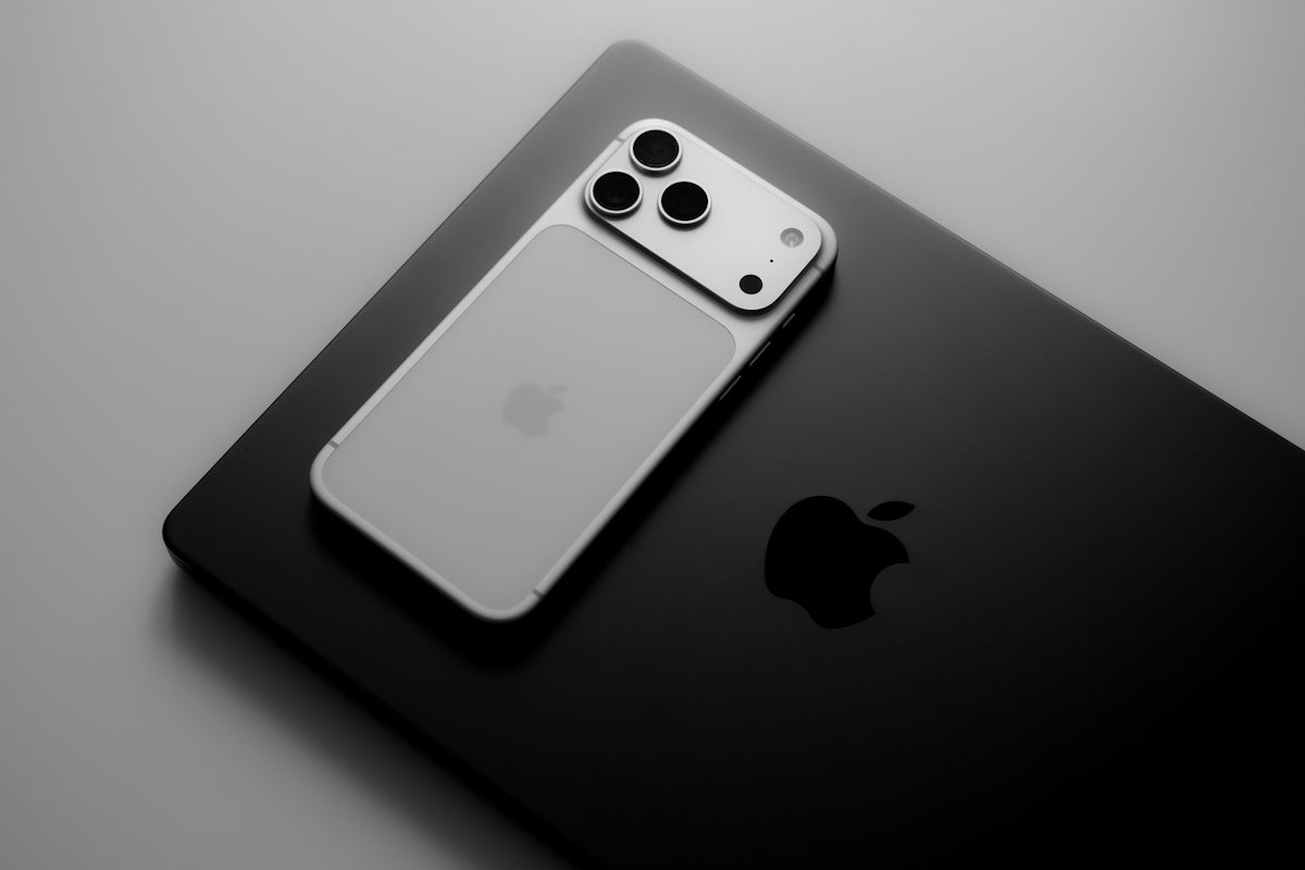 Smartphone resting on laptop with apple logos.